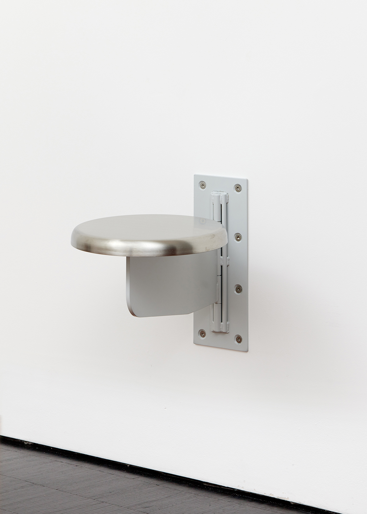 Ein Metall-Hocker, der an der Wand befestigt ist. Das Kunst-Werk ist von der Künstlerin Sung Tieu.